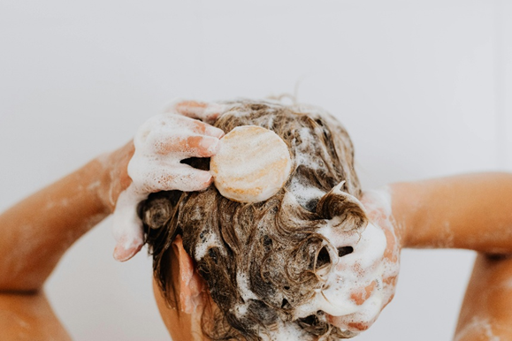 Personne se lavant les cheveux avec un shampoing solide, créant une mousse abondante sur cheveux mouillés.


